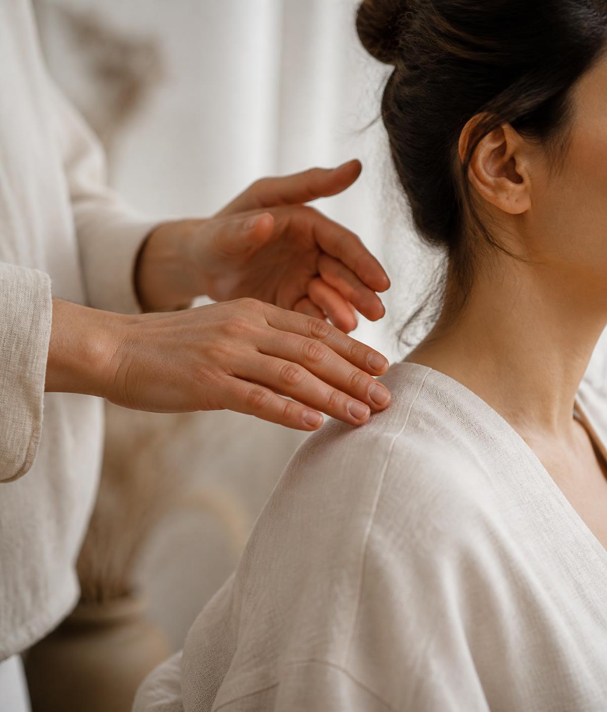 Terapeuta conduzindo uma sessão de Reiki com as mãos próximas ao ombro da pessoa atendida